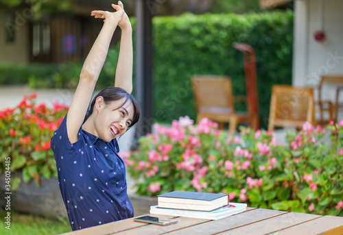 Young Asian girl in blue shrit stretching her arms while reading books at the garden bench. relaxing at home photo