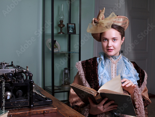 Young woman in blue vintage dress late 19th century reading the book in retro room photo