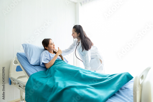 Obraz na płótnie Asian young female patient on bed showing thumbs up with smiley face very good symptom to asian young female doctor in hospital background. w salonie