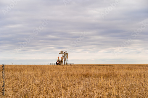 An oil well pump jack pumping on the prairie of Oklahoma during a cloudy day.