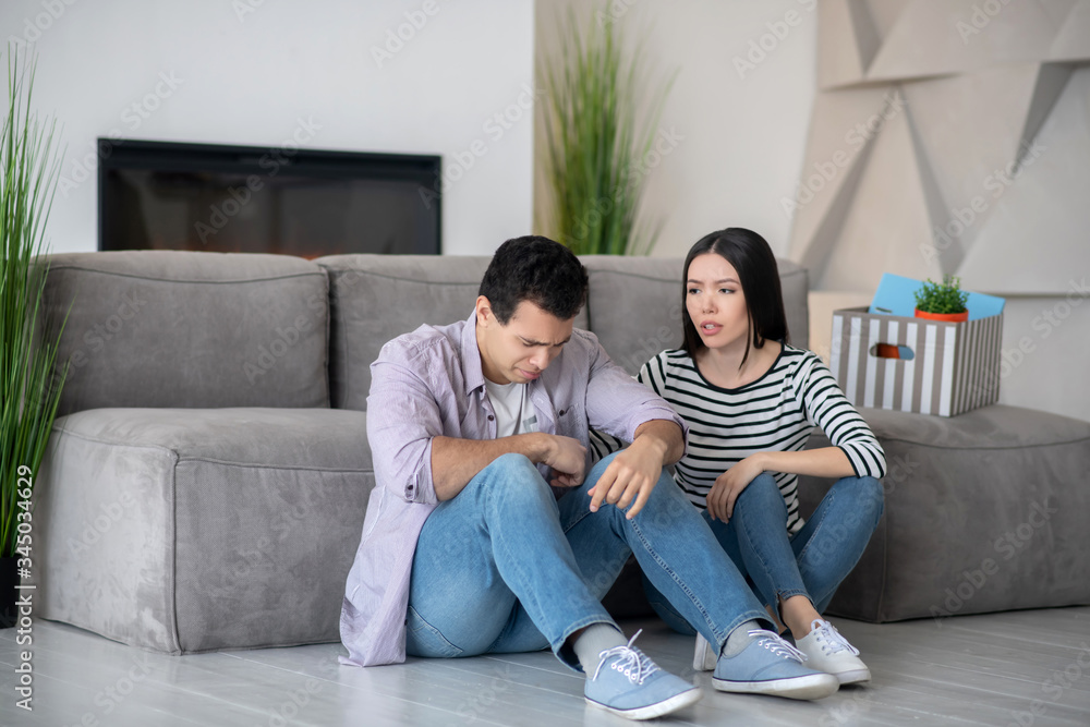 Unhappy young guy and long-haired wife are sitting on floor. Unhappy young guy and long-haired wife are sitting on floor.