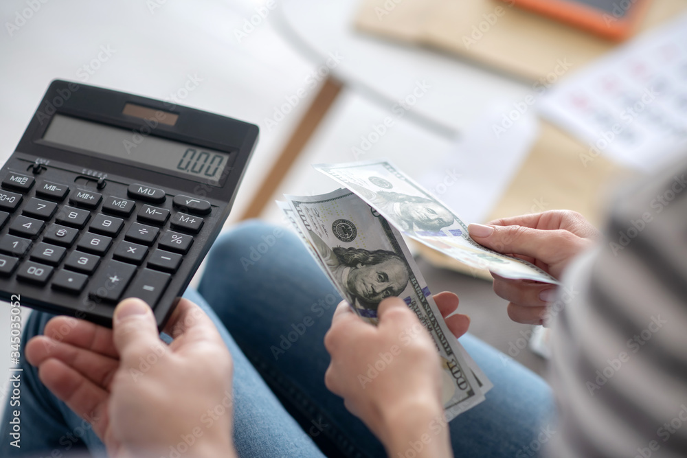 Fototapeta premium Male hand holding a calculator, female hands with dollar bills.
