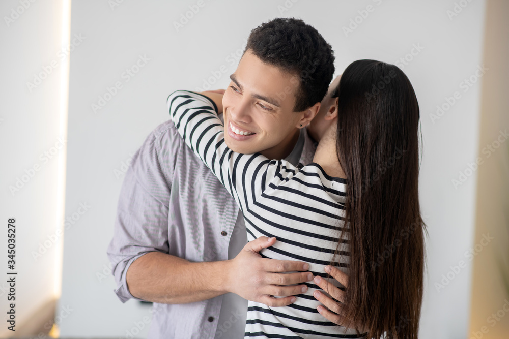 Young smiling dark-haired man hugging a woman. Young smiling dark-haired man hugging a woman.