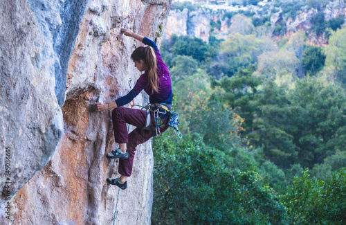 Fotografija A strong woman climbs a rock on the background of the forest.