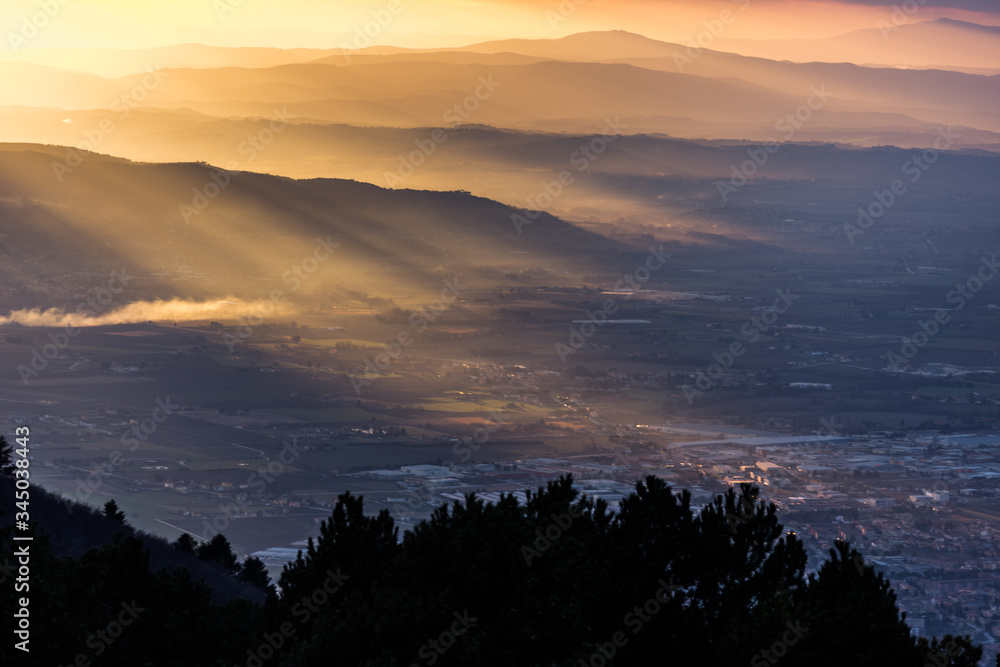 Sunrays at sunset above Umbria valley (Italy) cutting through the mist and hills