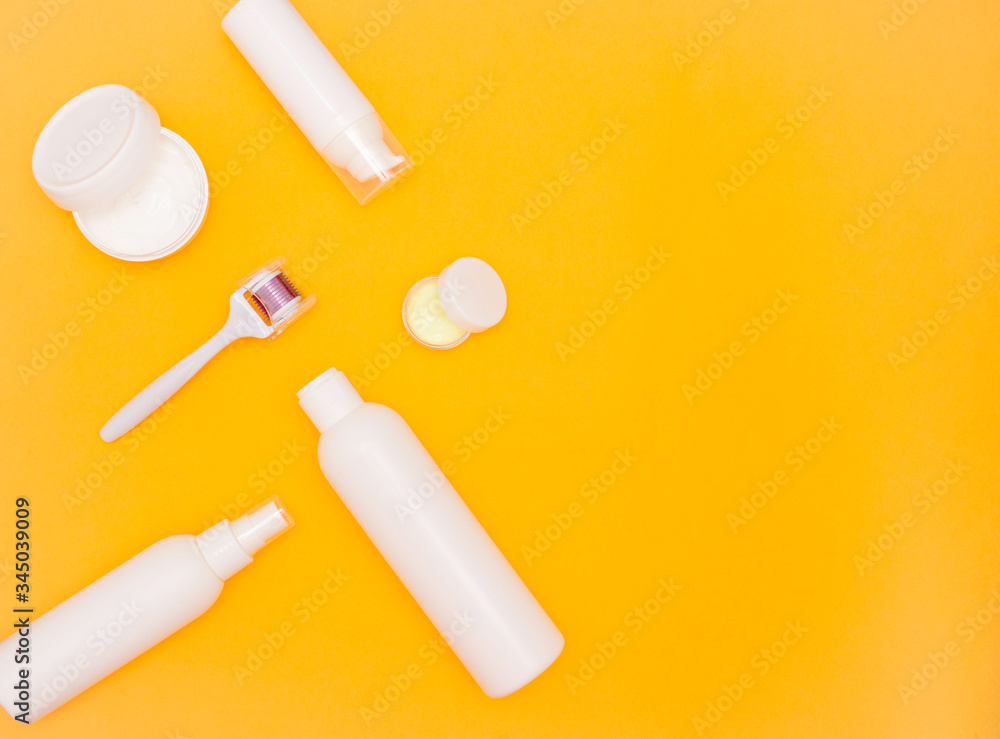 White plastic jars with cream and bottles of cosmetics on a bright background, a mesoroller and a branch with flowers. Top view, free space for text. Care cosmetics. White plastic jars with cream and bottles of cosmetics on a bright background, a mesoroller and a branch with flowers. Top view, free space for text. Care cosmetics.