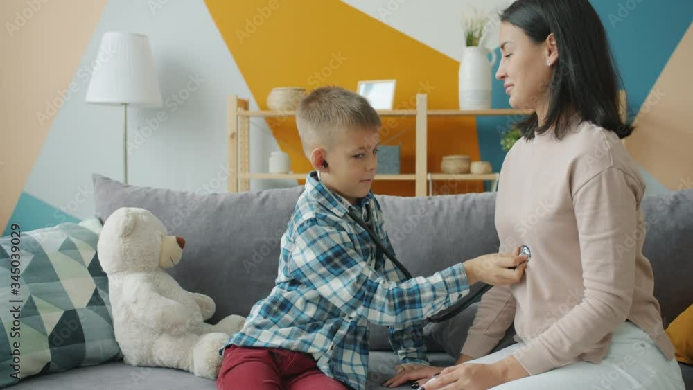 Cute little boy is examining mother with stethoscope playing doctor game in apartment having fun together. Childhood, healthcare and medical activities concept. Cute little boy is examining mother with stethoscope playing doctor game in apartment having fun together. Childhood, healthcare and medical activities concept.