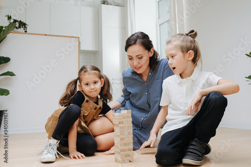 Mom and children playing popular game with wooden blocks  building high tower