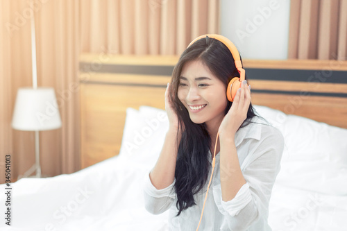 Asian beautiful woman resting in bed using headphone listening to music on wireless headset tablet surfing internet in bedroom comfortably relaxing smiling enjoying carefree lifestyle holiday weekend