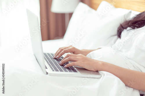 Asian beautiful woman resting in bed using computer laptop surfing internet working planning in bedroom comfortably relaxing smiling enjoying morning sunshine carefree time of holiday vacation