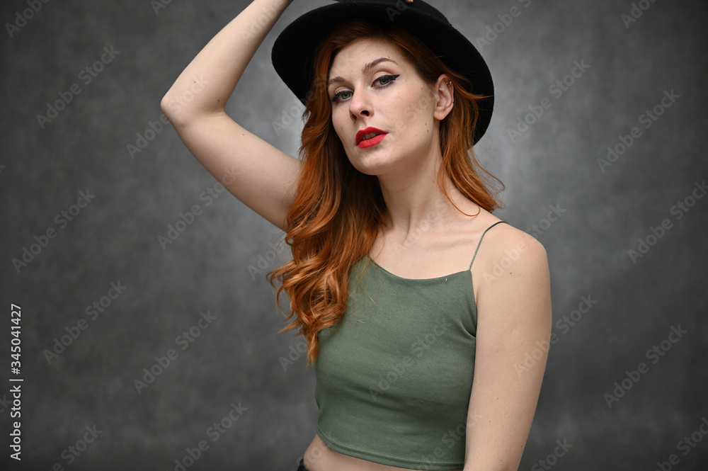 Woman shows emotions changing poses. Portrait of a young pretty girl with beautiful hair and great makeup in a green T-shirt and black hat on a gray background. Woman shows emotions changing poses. Portrait of a young pretty girl with beautiful hair and great makeup in a green T-shirt and black hat on a gray background.