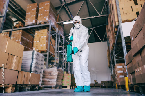 Photography Man in protective suit and mask disinfecting warehouse full of food products from corona virus / covid-19