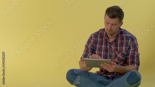 Close-up of Intelligent young man working on tablet on yellow background. He sitting on the floor. © art24pro