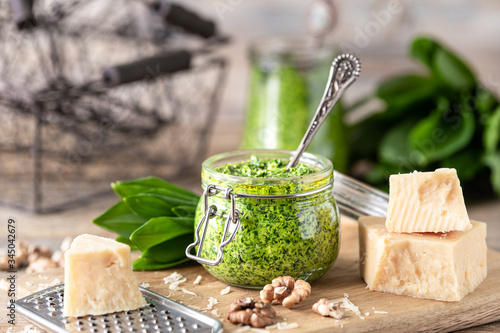 Wild leek pesto with olive oil and parmesan cheese in a glass jar on a wooden table. Useful properties of ramson. Leaves of fresh ramson. photo