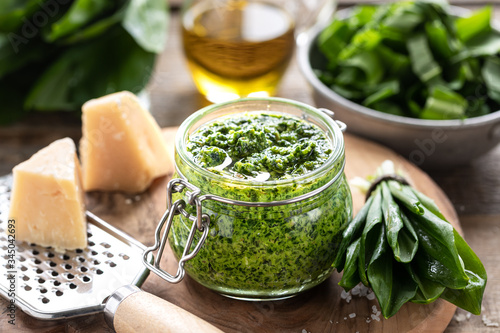 Fotografiet Wild leek pesto with olive oil and parmesan cheese in a glass jar on a wooden table