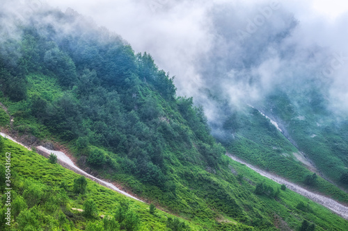 The green slopes of high mountains are hidden in clouds and fog. Melting snow in high mountains in summer