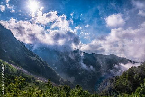Heavy fog, clouds and bright blue sky with the sun in mountains in the summer or spring. A layer of melting snow in the summer in high mountains.