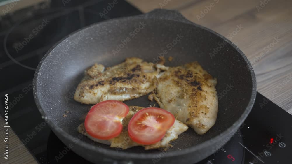 Woman fries fish in a pan with tomatoes and grated cheese Woman fries fish in a pan with tomatoes and grated cheese