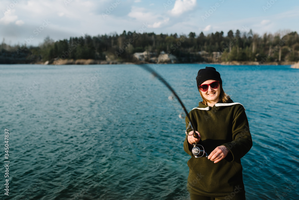 Fisherman with rod, spinning reel on river bank. Sunrise. Fishing for pike, perch, carp. The concept of rural getaway. Woman catching fish, pulling rod while fishing from lake or pond with text space.