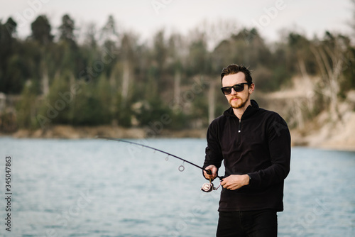 Fisherman with rod, spinning reel on the river bank. Man catching fish, pulling rod while fishing from lake or pond with text space at weekend. Fishing for pike, perch, carp on beach lake or pond. © Serhii