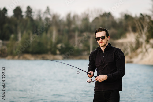 Fisherman with rod, spinning reel on the river bank. Man catching fish, pulling rod while fishing from lake or pond with text space at weekend. Fishing for pike, perch, carp on beach lake or pond.