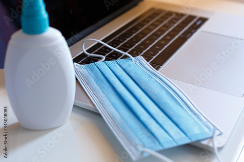 Mascherina chirurgica e spray antibatterico sopra un computer portatile photo