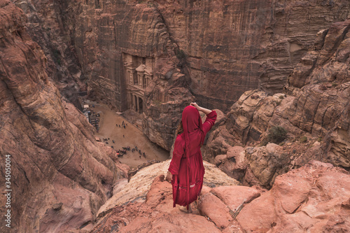 A woman traveller wearing red dress standing on top of mountain looking to the Treasury in Petra ancient and ruin city, Jordan