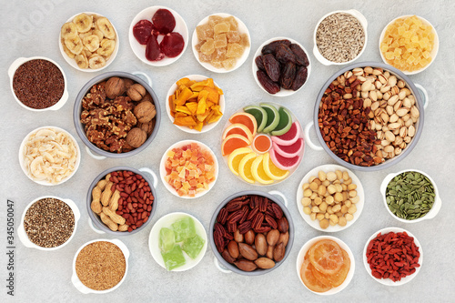 Healthy vegan dried fruit, nut & seed collection. High in antioxidants, protein, omega 3, minerals, vitamins & anthocyanins. Flat lay on mottled grey background.