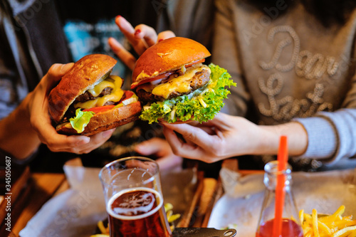 Woman and man hold burgers in their hands. Fresh burger cooked on a barbecue in kraft paper. American food. Nearby are drinks.