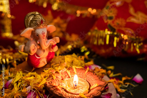 high angle shot of lord ganesha statue with terracotta lamp on rose petals against blurred background. religion concept.