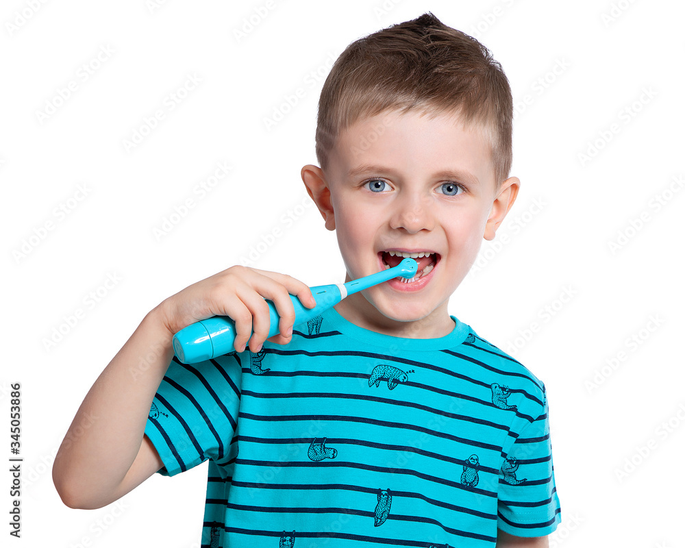 A beautiful European boy brushes his teeth with an electric toothbrush and smiles. Care for the oral cavity. Pediatric dentistry. Beautiful baby teeth. On white background. A beautiful European boy brushes his teeth with an electric toothbrush and smiles. Care for the oral cavity. Pediatric dentistry. Beautiful baby teeth. On white background.