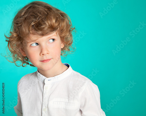 фотографія A beautiful curly-haired, blue-eyed boy looks slyly, incredulously, mysteriously to the side