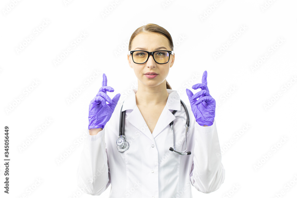 young female doctor in glasses with stethoscope looks at camera holding her hands up in blue gloves pointing her index fingers up isolated on white background copy space. Danger warning concept young female doctor in glasses with stethoscope looks at camera holding her hands up in blue gloves pointing her index fingers up isolated on white background copy space. Danger warning concept