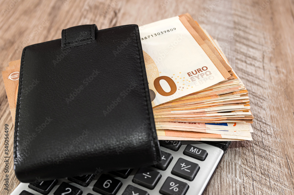 A lot of euro banknotes in a black wallet on a calculator. Close-up. 50 euros in the wallet. A lot of euro banknotes in a black wallet on a calculator. Close-up. 50 euros in the wallet.
