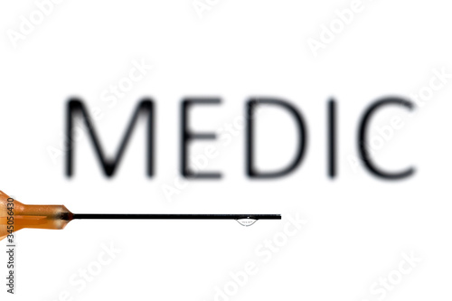 A medical needle with a droplet suspended refracting the word medic, which is also out of focus in the background