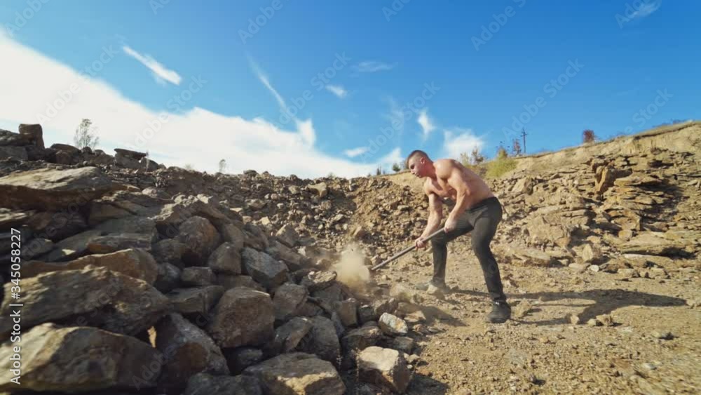 Sportsman with hard hammer on the rocky background. Athletic man without shirt breaking stones with metal hammer outdoors. Slow motion. Sportsman with hard hammer on the rocky background. Athletic man without shirt breaking stones with metal hammer outdoors. Slow motion.
