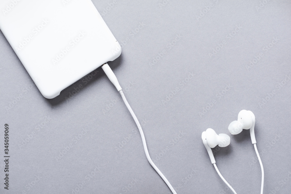 Modern White earphones and mobile phone on a gray background. Minimalist style. Top view with copy space. Modern White earphones and mobile phone on a gray background. Minimalist style. Top view with copy space.