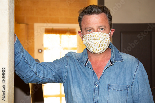 man with protective face mask handmade looking against coronavirus in home interior photo