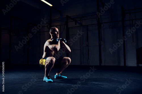 Athletic man doing squats with kettlebells exercise at gym