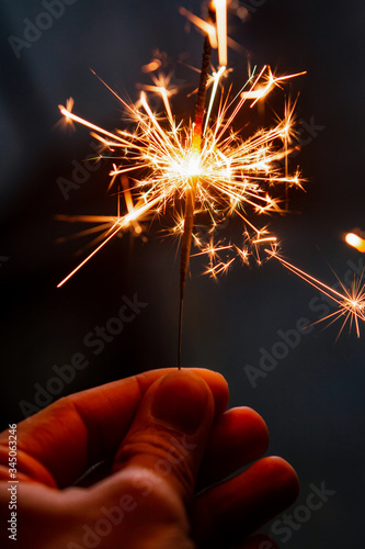 Female hand holding a burning sparkler, Christmas and new year sparkler holiday background