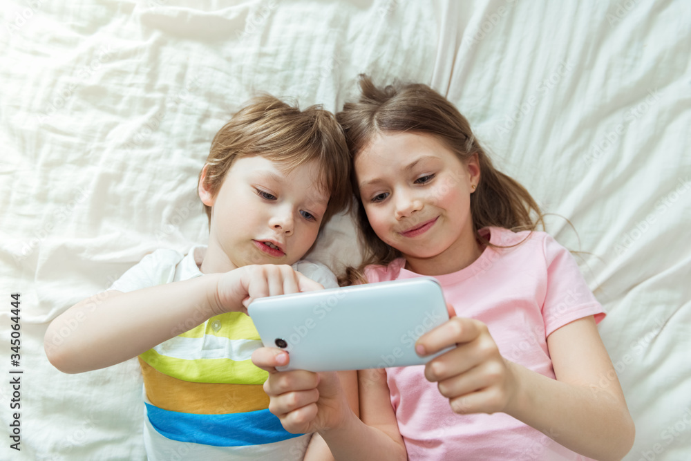 Happy children watching online movie stream with digital mobile tablet and lying on bed at home in morning, video call connection, social distancing, network technology concept Happy children watching online movie stream with digital mobile tablet and lying on bed at home in morning, video call connection, social distancing, network technology concept