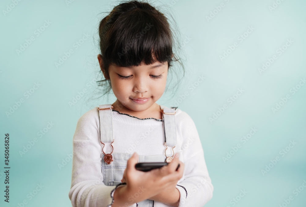 Smiling cute asian child girl using smartphone to play internet and play social media connection such as facebook, twitter, instagram and sending SMS, chatting with friend. Technology concept. Smiling cute asian child girl using smartphone to play internet and play social media connection such as facebook, twitter, instagram and sending SMS, chatting with friend. Technology concept.