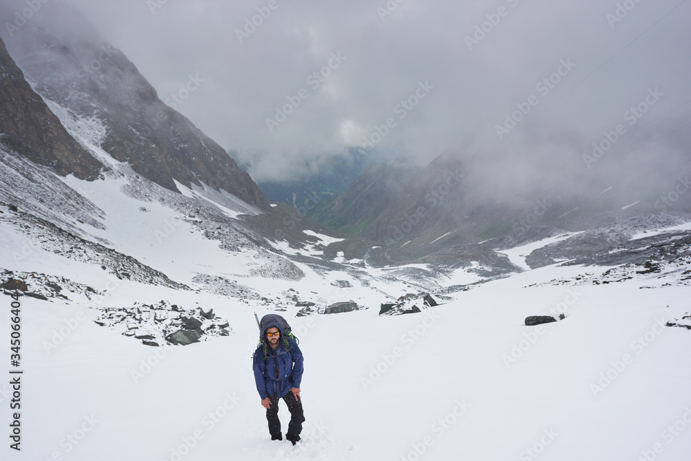 Beautiful view of winter mountains with male traveler. Tourist in hiking sunglasses standing on snow covered path with fantastic foggy hills on background. Concept of travelling, hiking and alpinism.