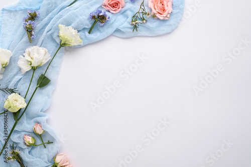 flower composition of rose buds, eustoma, lemongrass inflorescences on blue gauze and white background, copy space, top view, space for text