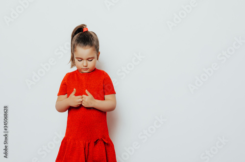 shy child girl in a red dress looks bottom. girl posing in studio     photo