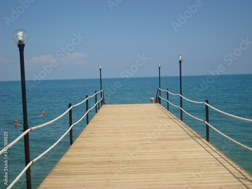Wooden bridge with rope railing on the blue sea. Beautiful pier with lanterns for evening walks and diving. Blue sky and calm sea.
