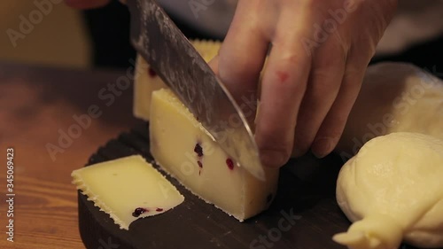 A chef cuts cheese on a black cutting board. photo