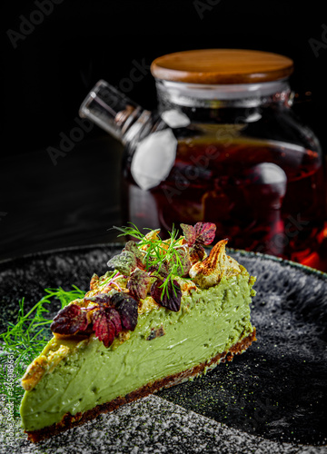 Close up view of a piece of pistachio cheesecake in plate on black wooden table background