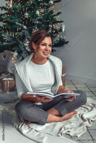 A girl sits under a Christmas tree and opens gifts for the New Year and Christmas.