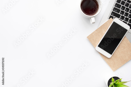 White office desk table with smartphone with blank mockup screen, laptop computer, cup of coffee and supplies. Top view with copy space, flat lay.